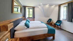 Une chambre avec un grand lit, deux chaises, une petite table et une fenêtre avec des rideaux.