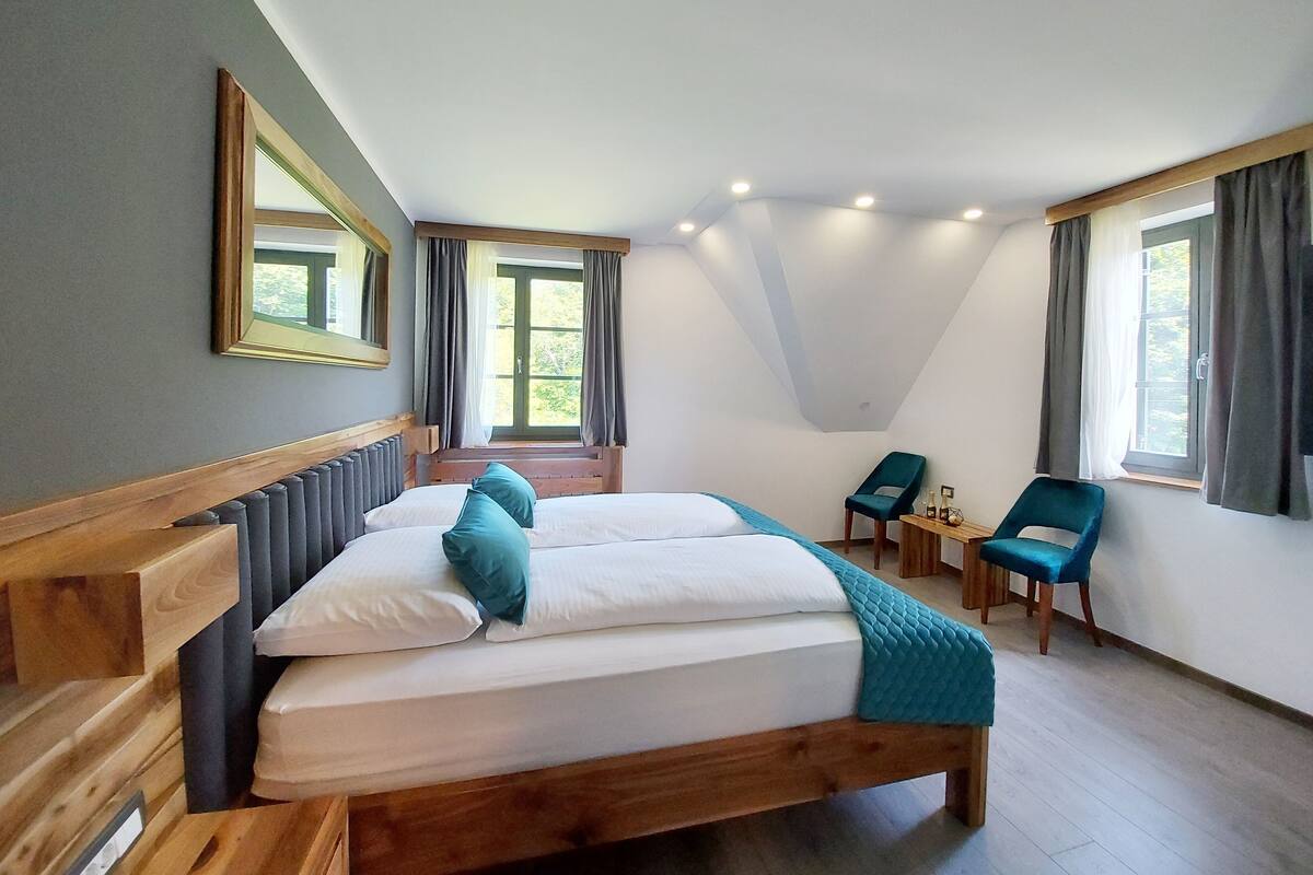 A bedroom with a large bed, two chairs, a small table, and a window with curtains.