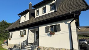 Une maison à deux étages, avec des fondations en pierre, un toit en tuiles et un porche à l’avant, accessible par quelques marches menant à une porte.