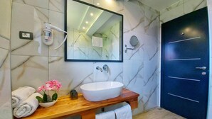 Une salle de bain moderne avec un pare-feu en marbre, un lavabo blanc, un miroir et une porte sombre.