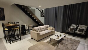 A modern living room with a sofa, coffee table, ottoman, and a staircase. - Ebs properties  (Accra)