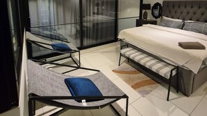 A modern bedroom with a large bed, a glass partition, a sofa, and a bench. - Ebs properties  (Accra)