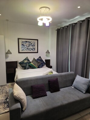 A modern bedroom with a bed, a grey sofa, and a ceiling light fixture. - Ebs properties (Accra)