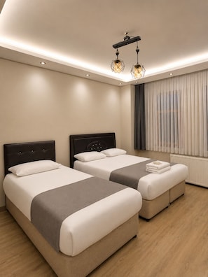 A modern hotel room with two beds, a large window with curtains, a ceiling light fixture, and a radiator. - Uzungol Dear Otel (Caykara)