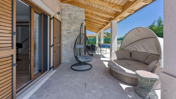 Eine Terrasse im Freien mit Holzboden, einem Hängesessel, einem runden Tisch und einer Couch.