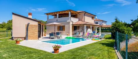 A two-story house with a swimming pool, outdoor seating, and a fenced yard.