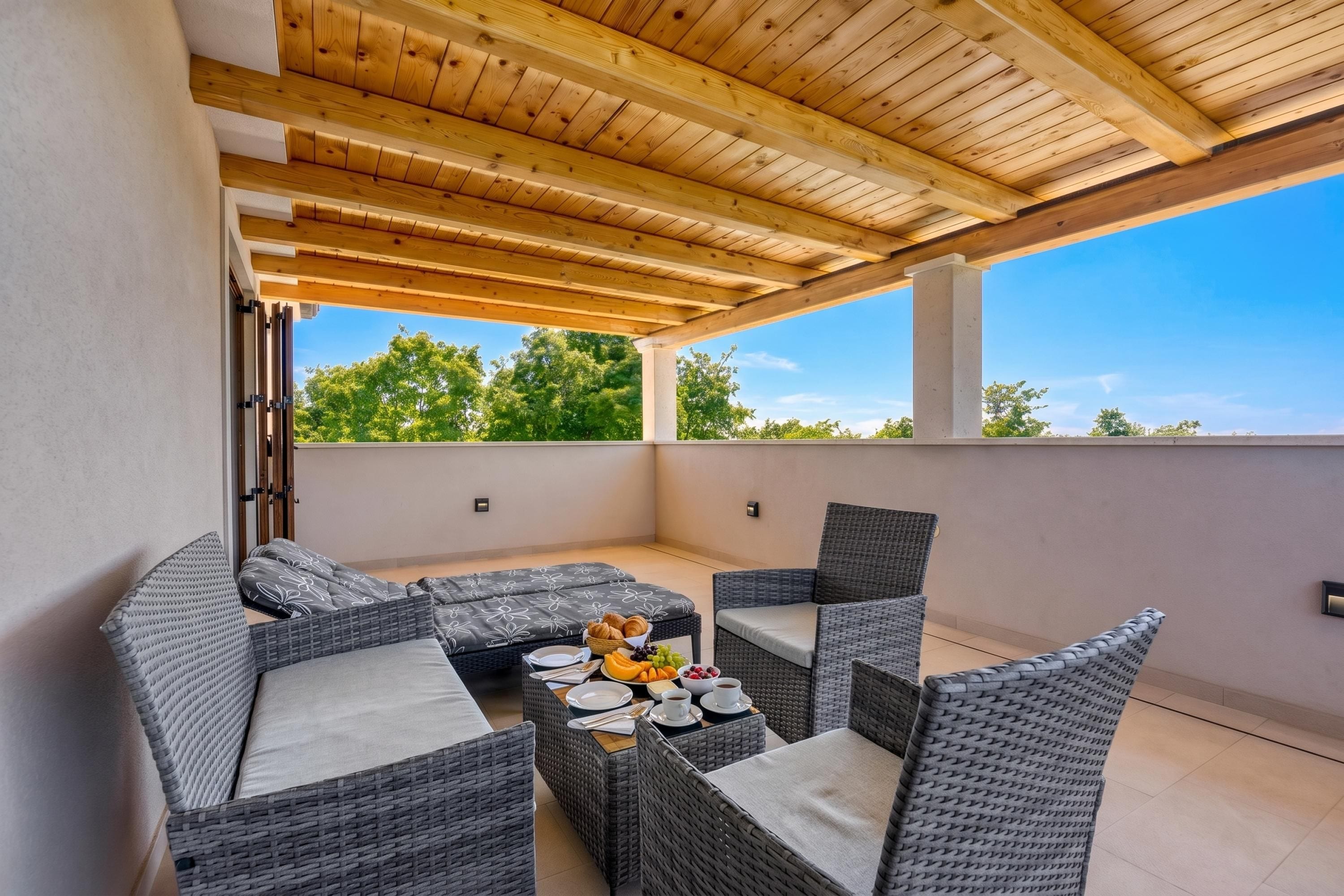 A covered outdoor seating area with wicker furniture and a table set for breakfast.
