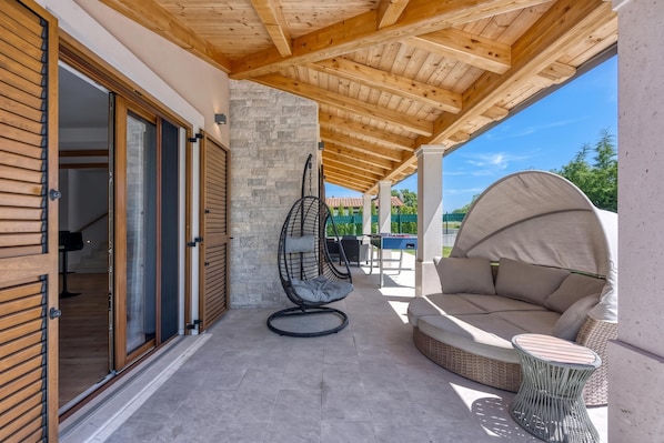 A covered outdoor patio with a wooden ceiling, a stone wall, a swing chair, a sofa, and a table. - Pool and Fun Villa Stella Klarici (Svetvincenat)