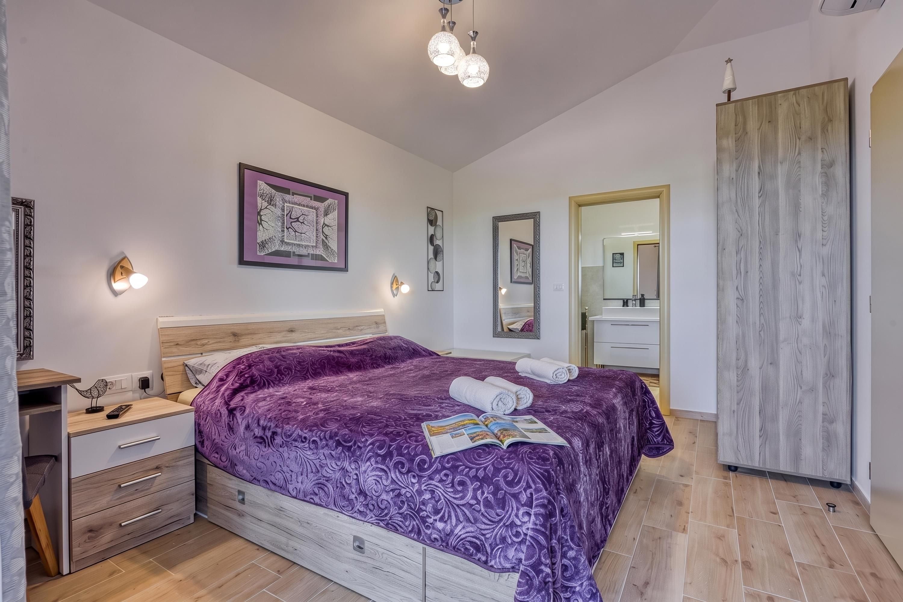A bedroom with a large bed, bedside tables, a dresser, a wardrobe, and a mirror.