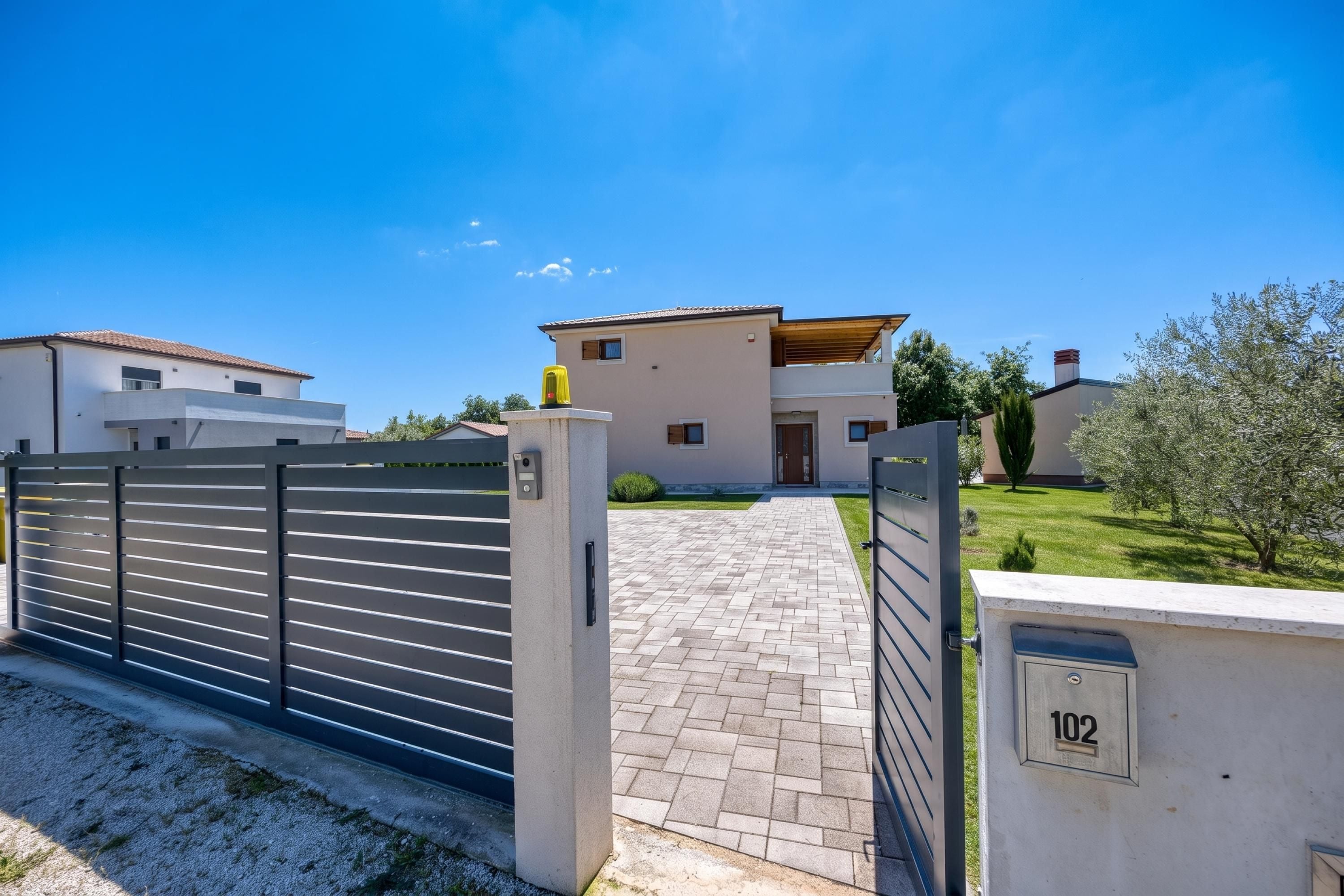 A gated residential area with a paved driveway leading to a modern two-story house.