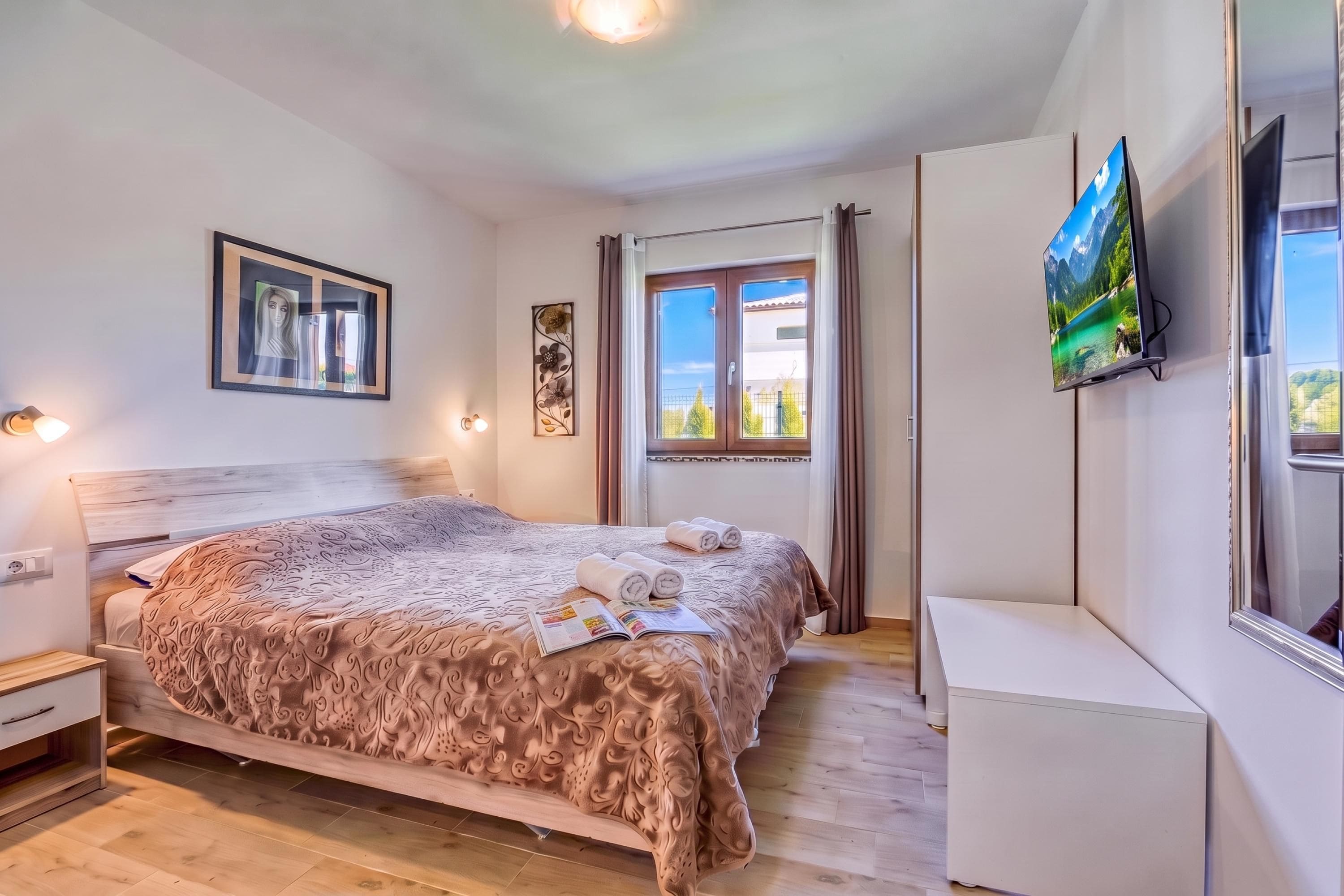 Un dormitorio con cama, televisión, ventana y puerta.