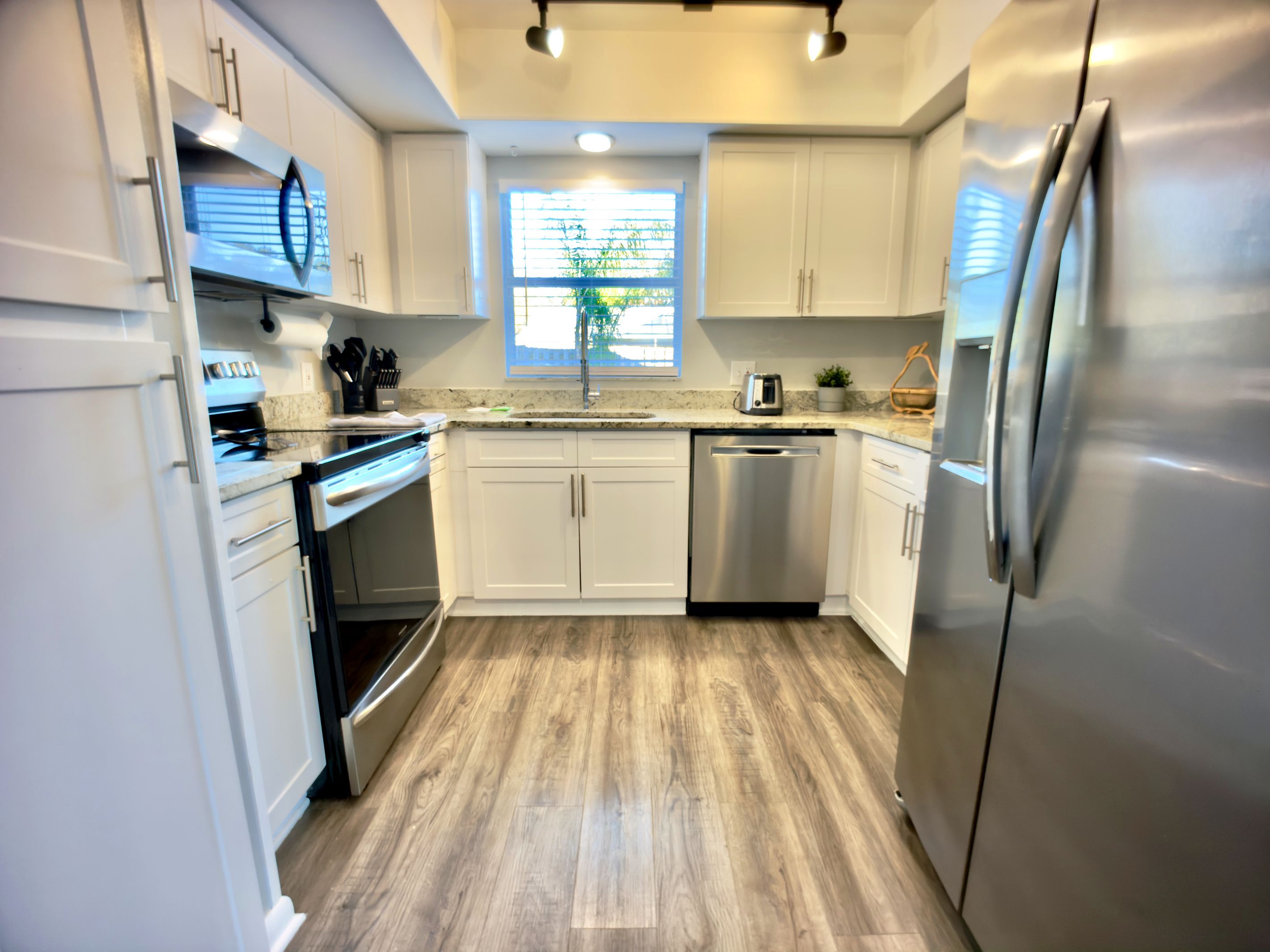 A modern kitchen with white cabinets, stainless steel appliances, and a wooden floor.