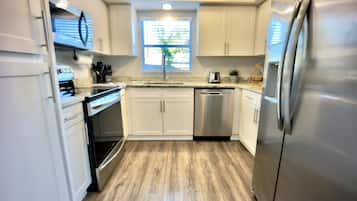 A modern kitchen with white cabinets, stainless steel appliances, and a wooden floor.