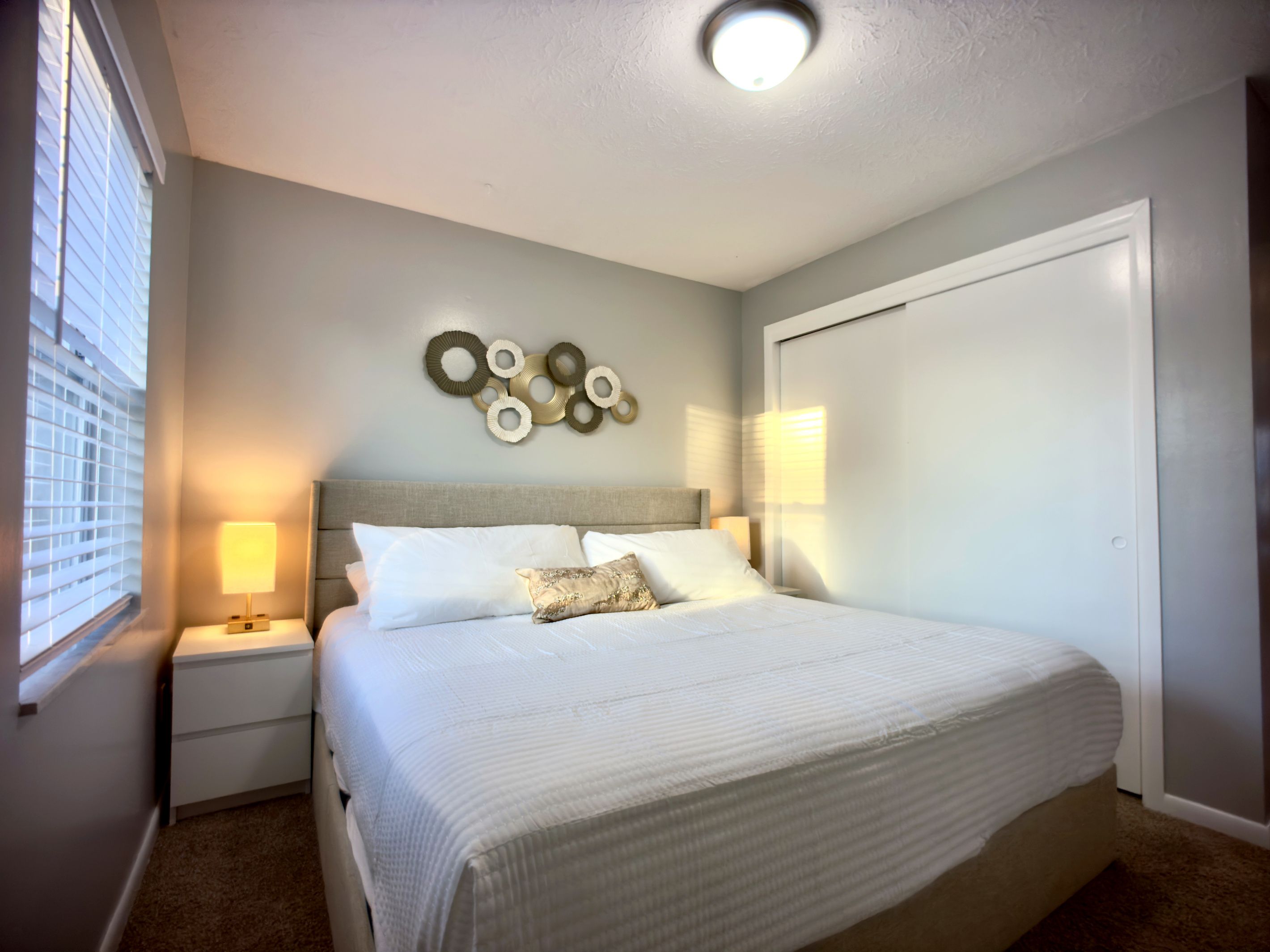 A bedroom with a large bed, bedside tables, a wall-mounted light fixture, and a door.