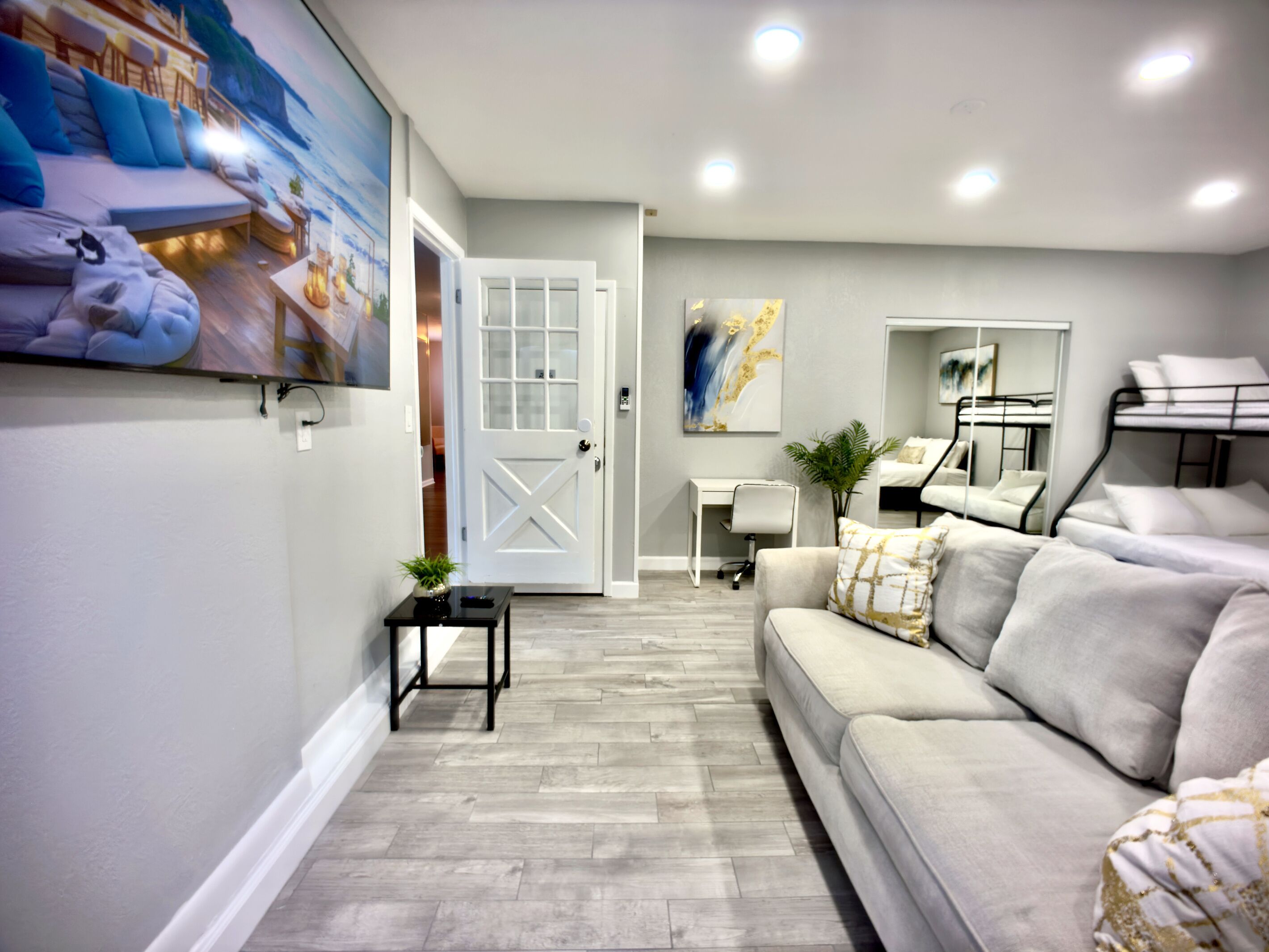 A modern living room with a sofa, a small table with a plant, a desk, and a bunk bed.