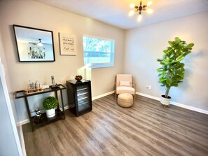 A room with a wooden floor, a ceiling fan, a wall-mounted projector, a potted plant, a chair, and a console table with decorative items. - Heated Pool & Basketball, Sleeps 12 | Tropical Dream Villa, Valrico / Brandon (Valrico)