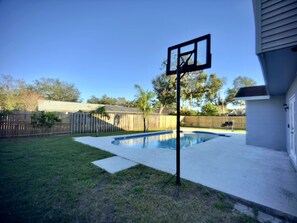 A backyard with a swimming pool, a basketball hoop, and a wooden fence. - Heated Pool & Basketball, Sleeps 12 | Tropical Dream Villa, Valrico / Brandon (Valrico)
