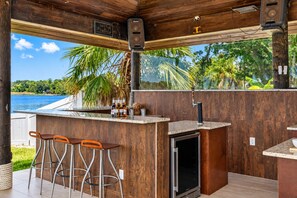 An outdoor bar area with a view of a lake, wooden walls, and a bar stool setup.
