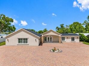 A two-story house with a brick driveway and a landscaped garden in front. - Stunning 5-Bedroom Lakefront Retreat! (Tampa)
