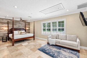 A bedroom with a four-poster bed, a sofa, a large window with blinds, and a flat-screen TV mounted on the wall.