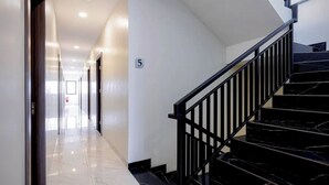 Un pasillo moderno de hotel con piso de mármol, una escalera negra con barandillas de metal y el número 5 en la pared.