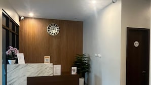 Zona de recepción con un mostrador de mármol, un panel de pared de madera, un reloj y una puerta con un letrero.