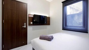 Una habitación de hotel con cama, televisor montado en la pared, ventana con vista a un edificio y armario de madera.
