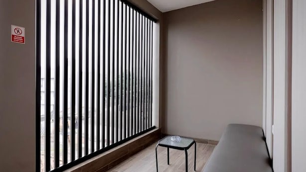 Habitación de esquina con puerta de vidrio corrediza, una mesita y un banco.