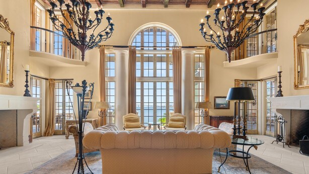 A spacious living room with a large sofa, two armchairs, and a coffee table. There are two chandeliers, a fireplace, and large windows with curtains. - Villa Grande (Orange Beach)
