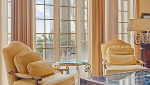 A room with two beige armchairs, a small round table with a glass top, and a lamp on a wooden side table. - Villa Grande (Orange Beach)