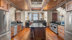 A spacious kitchen with a large island, wooden cabinets, stainless steel appliances, and a vaulted ceiling. - Villa Grande (Orange Beach)