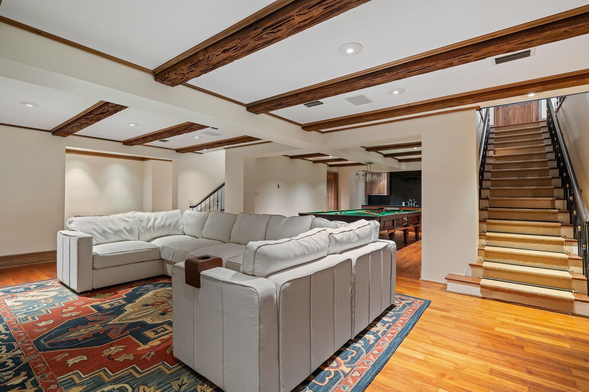 A modern living room with a sectional sofa, a pool table, and a staircase.