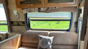Een gezellig interieur van een camper met een bank, een klein houten tafeltje en een raam met uitzicht op groen.
