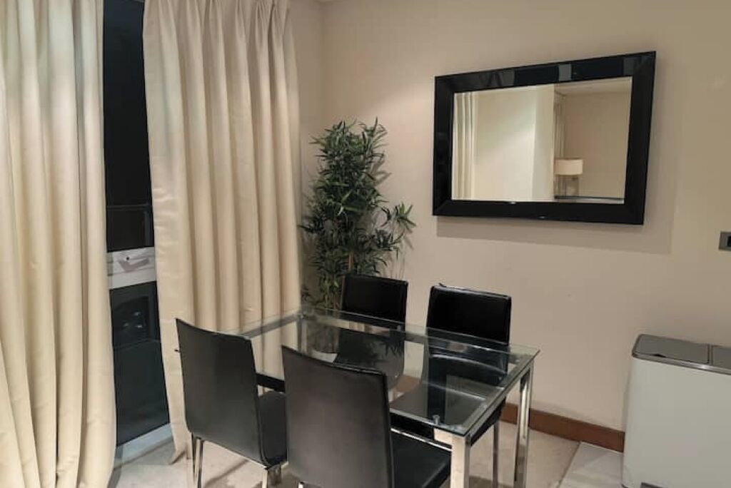 Un espace repas moderne avec une table en verre et des chaises noires, une plante en pot et un grand miroir au mur.
