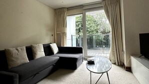 Een moderne woonkamer met een donkere bank, een klein rond tafeltje en een televisie.