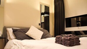 Een hotelkamer met een bed, een spiegel, een televisie en een stapel handdoeken.