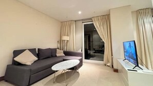 Een moderne woonkamer met een grijze bank, een klein wit bijzettafeltje en een televisie op een witte dressoir.