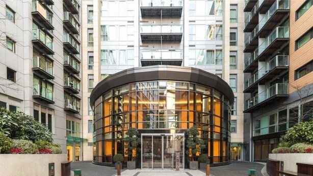 Een moderne hotelentree met een gebogen glazen gevel, een centrale ingang en een aangelegde omgeving.