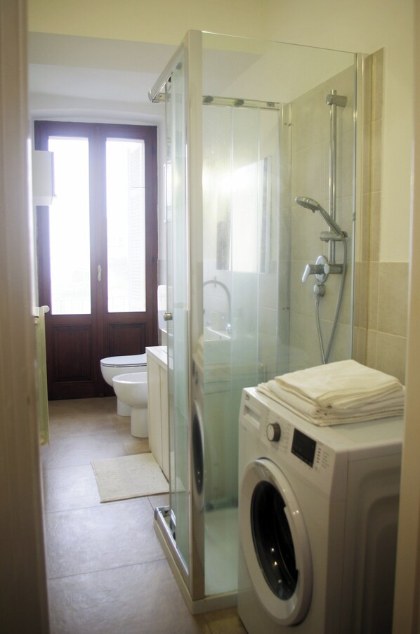 Un baño pequeño con cabina de ducha de vidrio, inodoro y lavadora y secadora apiladas.