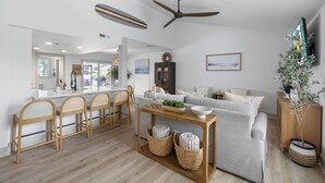 A modern living room with a sofa, a dining area with bar stools, a wooden coffee table, and a ceiling fan. - Bring your boat/Pool/Kayaks/Arcades (Hernando Beach)