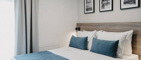A neatly made bed with a blue and white bedspread, a wooden headboard, and three framed pictures on the wall.