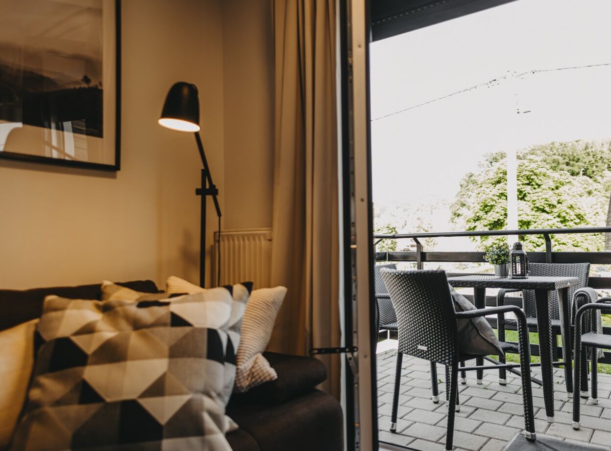 Una habitación acogedora con sofá, lámpara y vistas a un patio exterior con sillas y mesas.