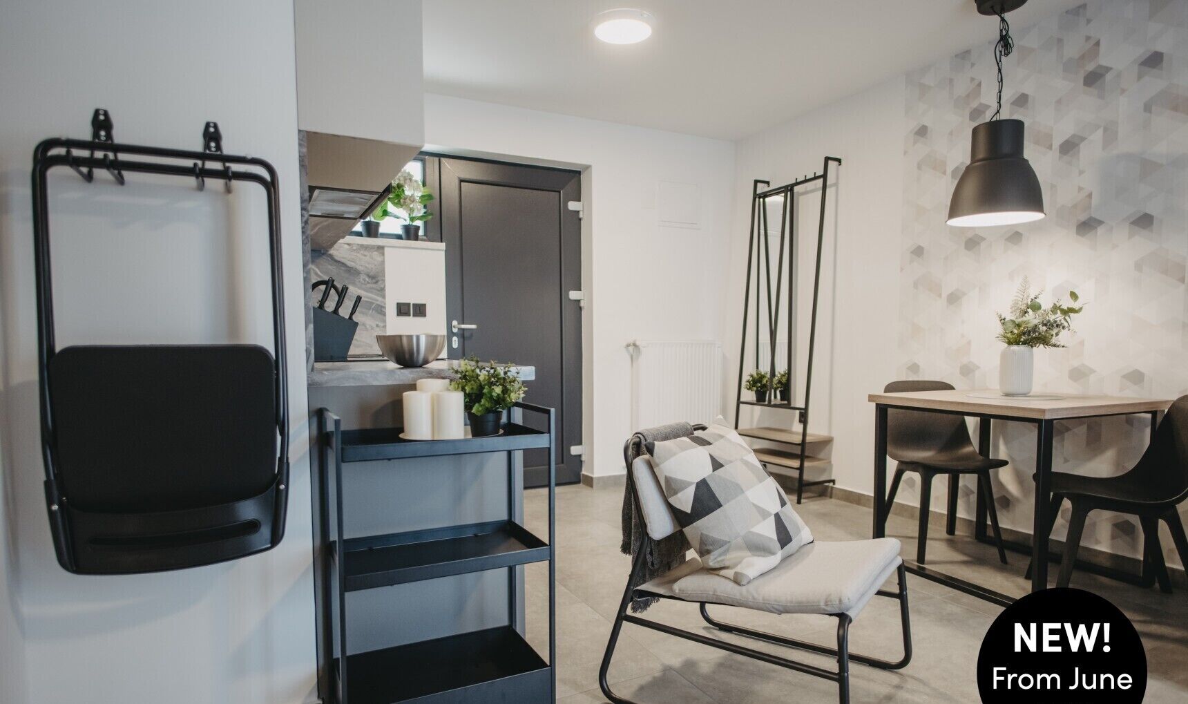 A modern kitchen with a black chair, a dining table, and a hanging light fixture.