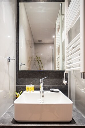 Een moderne badkamer met een grote spiegel, een witte wastafel en een zwart aanrecht.