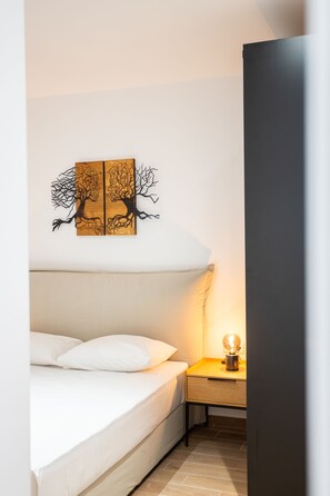 A bedroom with a bed, a bedside table with a lamp, and a wall-mounted artwork of two trees. - Exclusive 3-bedroom Haven in Kolonaki Center (Athens)