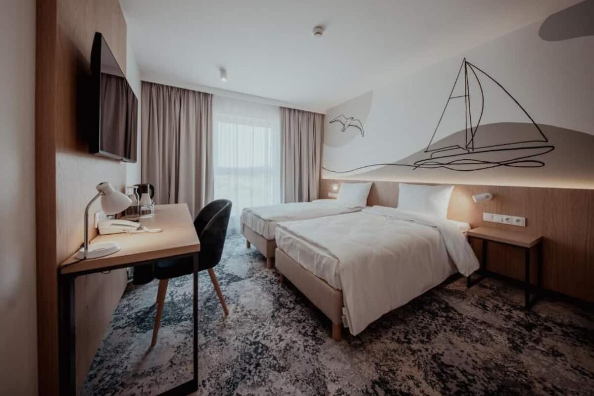 A hotel room with a bed, desk, chair, and a TV.