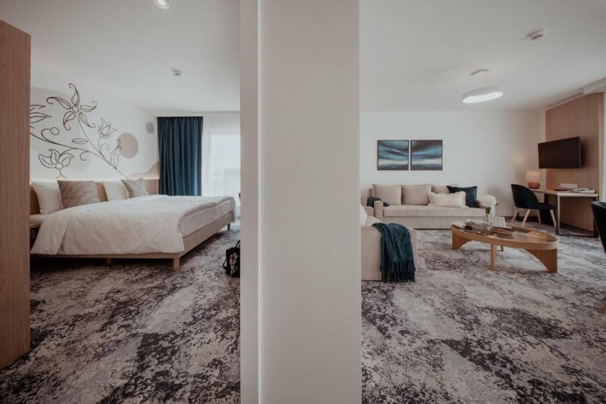A modern hotel room with a bed, a sofa, a coffee table, and a TV.