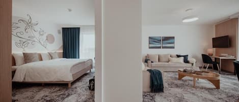 A modern hotel room with a bed, a sofa, a coffee table, and a TV.