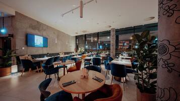 A modern restaurant with round tables, blue and red chairs, and large windows.
