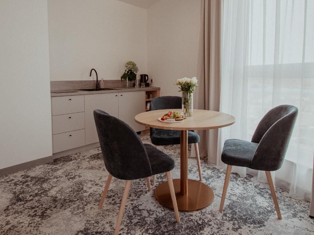 Una habitación moderna con una mesa redonda, dos sillas, una pequeña cocina y un ventanal con cortinas.